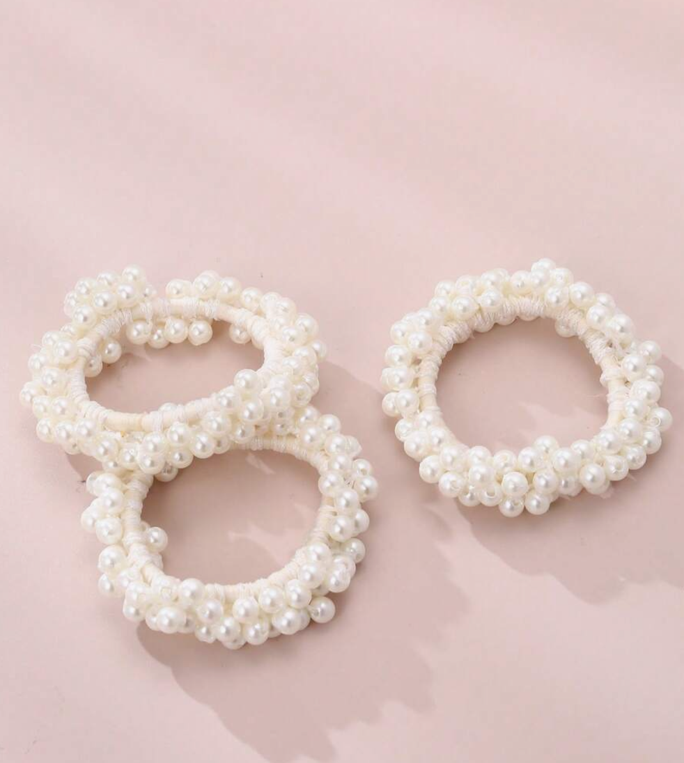 A close up of three of our Pearl Hairbands, spaced out against a pink background. Highlighting the size of each hairband and the cluster pearl design around the entire band, adding timeless charm to any occasion or must-have for brides or party-goers.