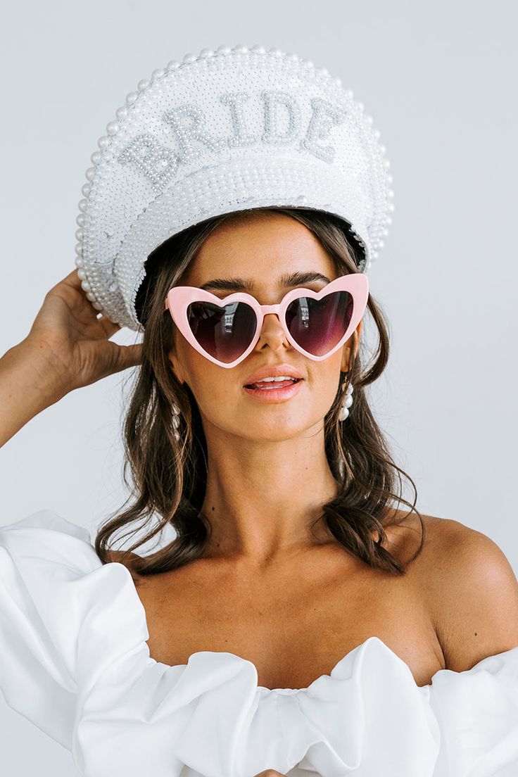 A bride to be wearing our Pink on Black Heart Sunglasses, with a bride hat on and white dress. These come in various colours, shown here are our pink with black lenses heart-shaped glasses. Perfect for bride or bridesmaids at your next hen party