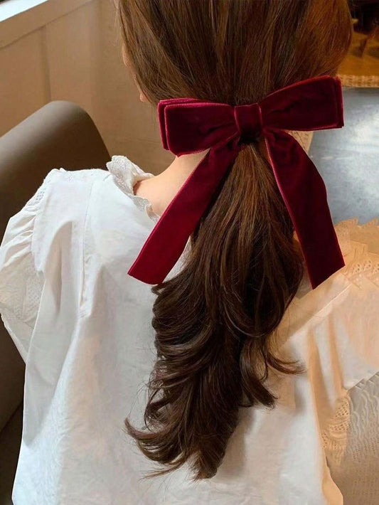 A woman wearing our Plum velvet bow hair clip, in a pony-tail style. Plush velvet material with a double layer of fabric at the top. Perfect for a wedding or a formal affair adding a luxurious touch.