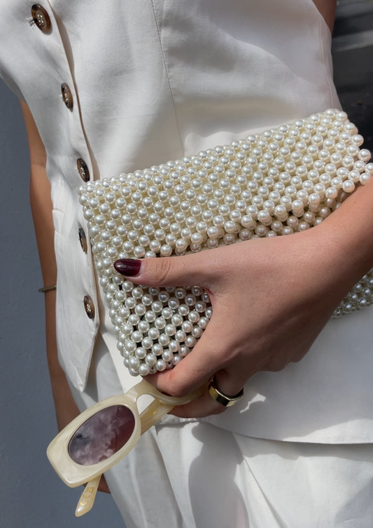 Woman holding our poppy bag as a clutch, without the pearl beaded shoulder attachment. She's holding sunglasses and wearing white, making the pearls really shine. Perfect for bride or bridesmaids at the wedding or parties 