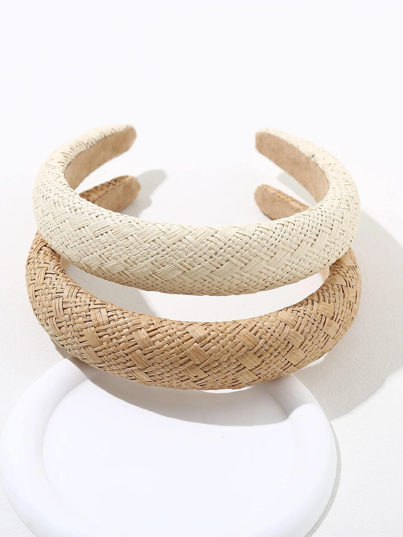 A stacked shot of two colour variations of our capri headband, cream at the top and natural straw brown on the bottom. Highlighting the woven design of the organic straw material variously sized across the padded band. Natural, fun and casual addition to any spring outfit 