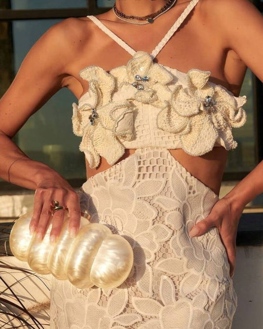 Woman wearing a white lace dress with floral embellishments, holding a gold clutch.