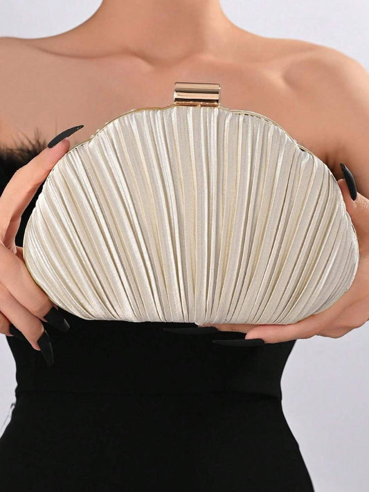 A woman holding our Audrey clutch bag, highlighting its compact size. This bag has a gold clasp at the top of the shell shaped satin clutch. It is a champagne colour which is accentuated by the woman's black dress in the background. Perfect for you next evening event.