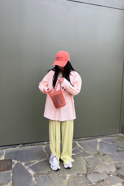 A woman holding our salmon/coral pink beaded bucket bag showing more of a size comparison. Paired with our spiced papaya Coral and Co faded orange denim cap with plum embroidery. The perfect match for a casual day to day look.