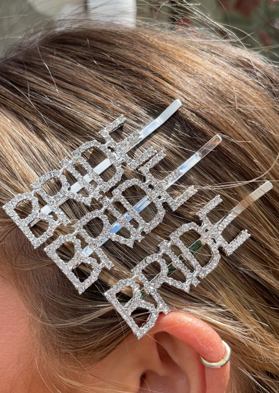 A close up of 3 of our 'Bride' Diamante Hair Clips, stacked in the hair above her ear. Showing the 'Bride' lettering and diamante rhinestone detail close up. Adding elegance and style to any bride's hair