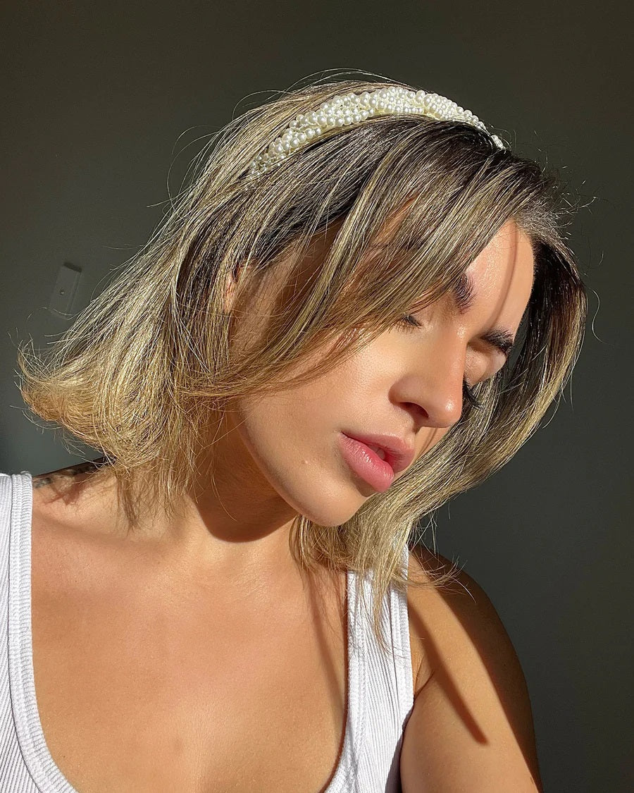 A woman wearing our Buttercup Headband, with braided small pearls, with short blonde/brunette hair in the sunlight. Showing how you can style this headband effortlessly with any outfit. Perfect for enhancing a day or evening outfit at your next event.